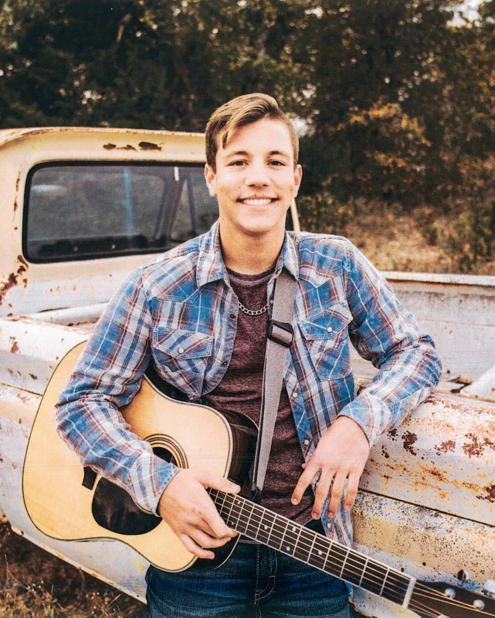 Nathan Sudderth, Cobell Undergraduate Scholar, holding an acoustic guitar beside a vintage pickup truck